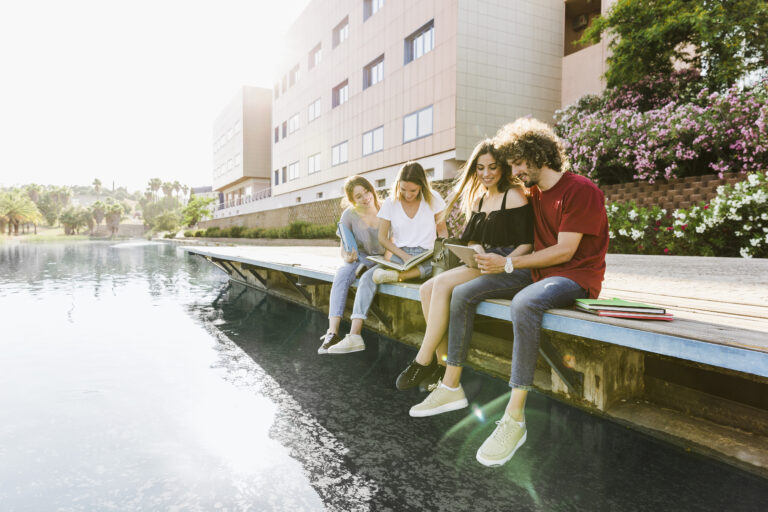 friends-studying-near-building-with-lake